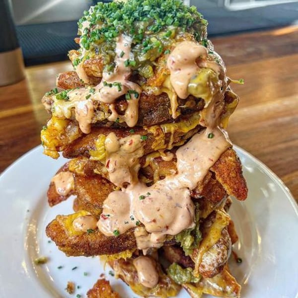 A towering stack of crispy potato wedges, melted cheese, and creamy sauce, topped with chives.