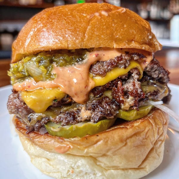A close-up of Jojo's double smash burger with melted cheese, pickles, and special sauce.