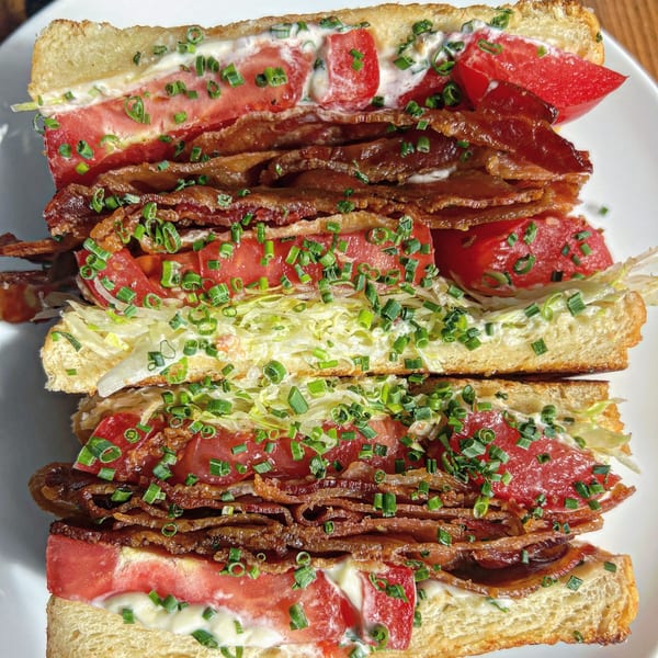 A Jojo sandwich with thick bacon, sliced tomatoes, lettuce, and chives on toasted bread.