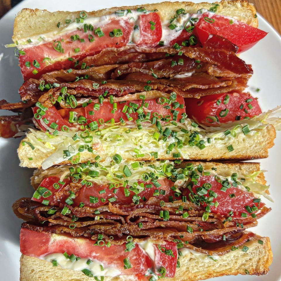 A Jojo sandwich with thick bacon, sliced tomatoes, lettuce, and chives on toasted bread.
