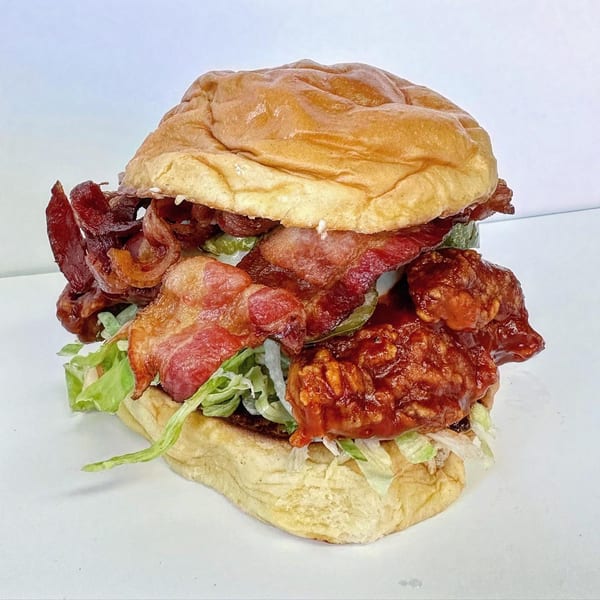 A Jojo sandwich with crispy bacon, saucy chicken, lettuce, and pickles on a brioche bun.