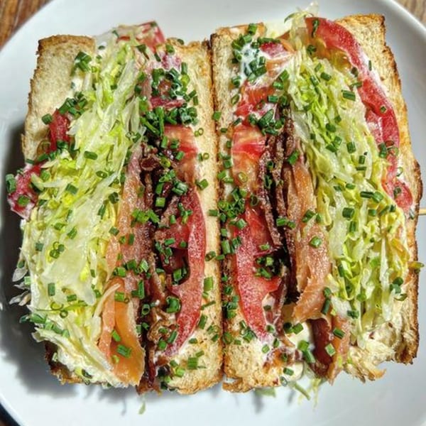 A Jojo sandwich, cut in half, filled with lettuce, tomatoes, bacon, and chives.