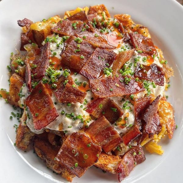 Crispy bacon, chives, and sauce topping a bed of golden-brown potatoes on a white plate.